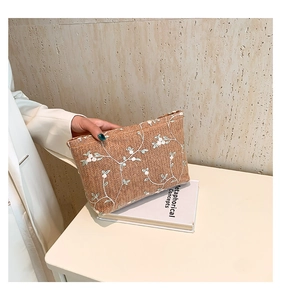 Detalle de bolso de paja trenzada con bordado de hojas verdes y flores blancas