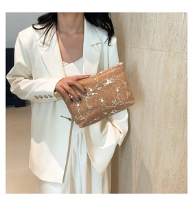 Detail of caramel straw woven clutch featuring white floral lace embroidery