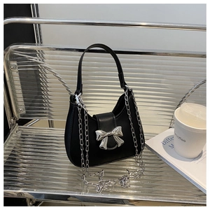 Détail du sac Hobo noir avec fermoir nœud en métal argenté sur un banc argenté