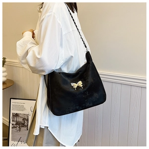 Detailed close-up of a black tote bag with a metal butterfly buckle and chain strap