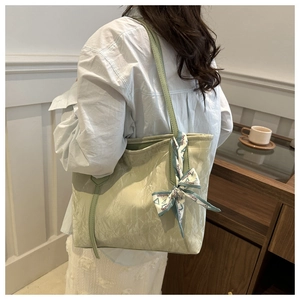 Detalle del bolso tote plisado verde claro con pañuelo decorativo llevado por una modelo