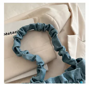 Detail of soft ruched handle on blue denim cloud bag with trendy pleated design