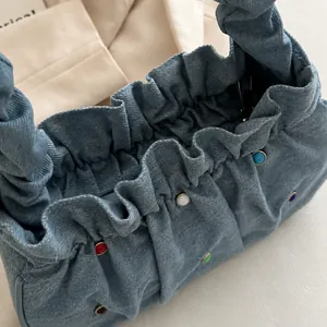 Detail of light blue denim handbag featuring colorful rivets and pleated elastic closure