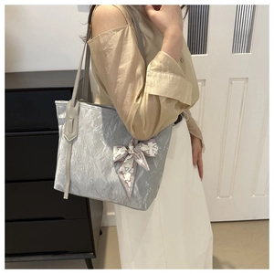 Detalle del bolso tote gris claro con textura arrugada y adorno de lazo negro