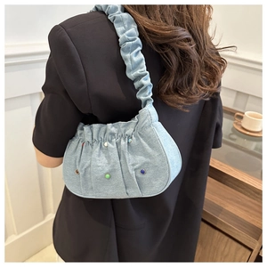 Detail of light blue denim cloud bag featuring colorful studs and pleated shoulder strap