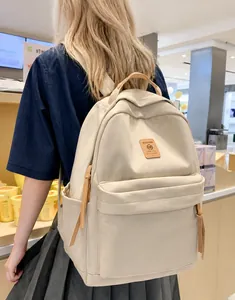 Detail view of a beige nylon backpack featuring brown leather straps and front pocket