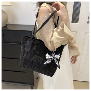 Detalle de bolso tote negro con textura plisada y adorno de cinta geométrica moderna