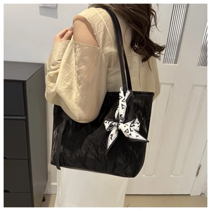 Detalle del bolso tote negro plisado con un pañuelo de seda decorativo en el asa superior