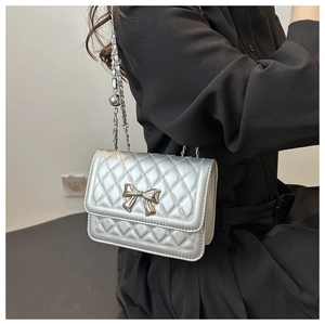 Detail der silbernen Stepptasche mit Metallschleife und dekorativem Kugelanhänger