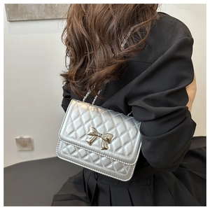 Silberne Stepptasche mit Metallschleife, getragen von einem Modell in schwarzem Kleid
