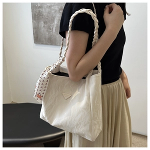 Detail of white pleated tote bag with braided handle and decorative silk scarf accessory