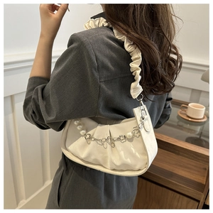 Detalle de bolso plisado blanco con cadena de perlas y adornos florales en la correa