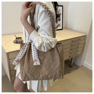 Detail of beige tote bag featuring pleated texture and silk scarf accessory on a shoulder strap