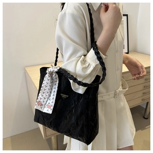 Detail of black textured tote bag with braided handle and patterned silk scarf accent