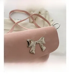 Detalle del bolso tipo cubo rosa con hebilla de lazo plateada y correa delgada