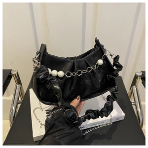 Detalle de bolso nube negro plisado con cadena de perlas y dijes de flores sobre libro