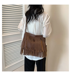 Detalle de bolso marrón con flecos bohemios en capas y correa de hombro trenzada fina