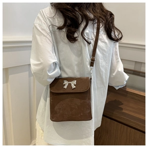 Bolso bandolera marrón con detalle de lazo plateado mostrado en modelo en un interior