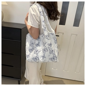 Détail du sac cabas montrant des broderies papillon bleues et une texture douce en peluche