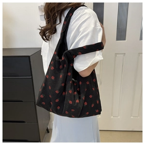 Detail shot of black corduroy tote bag featuring vibrant red strawberry pattern and soft texture