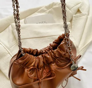 Détail du sac à cordon marron avec noeud latéral et bandoulière en chaîne argentée