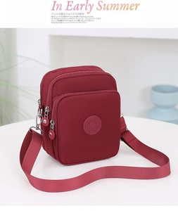 Detalle del bolso bandolera de nailon granate con tres compartimentos con cremallera y correa