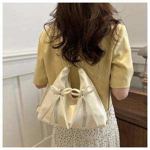Detail view of cream tote bag featuring decorative bows and side zipper on soft material
