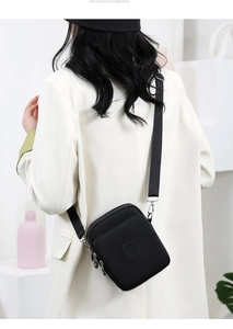 Detalle de un bolso bandolera de nailon negro con tres cremalleras y parche de logo