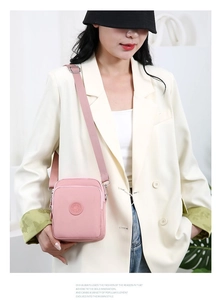 Detalle de bolso bandolera de nailon rosa con correa ajustable sobre blazer blanco