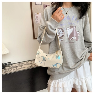 Close-up of beige shoulder bag with blue graffiti print and golden zipper detail