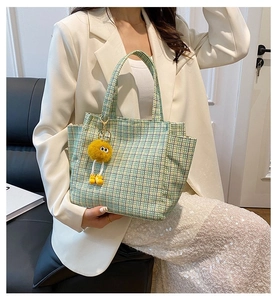 Detail of green and yellow knit tote bag featuring a cute plush pompom accessory