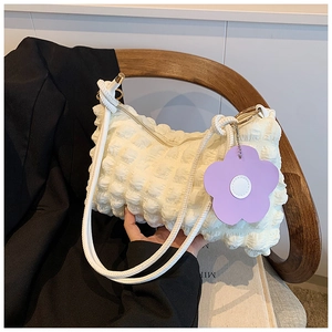Detail of off-white bubble texture fabric handbag with a purple floral pendant on a chair
