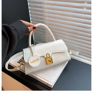 Close-up of white leather handbag featuring gold clasp and fashion charm on casual table