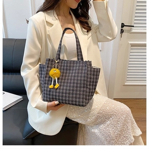 Detail of grey plaid knit handbag featuring a cute yellow plush doll charm accessory