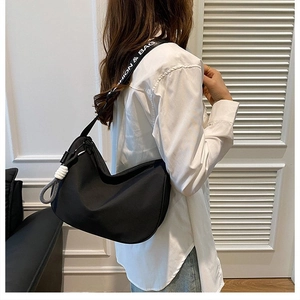 Detail der schwarzen Hobo-Tasche mit modischem Gurt und weißem Knotenhänger