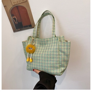 Detail of checkered knit tote bag with a cute yellow plush monster charm accessory
