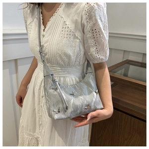 Detail of silver metallic hobo bag with butterfly hardware worn on white lace dress