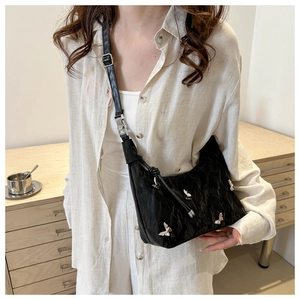 Detail of black pleated shoulder bag with silver butterfly charms worn on a cream shirt