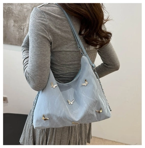 Detail of light blue pleated shoulder bag featuring decorative silver metal butterflies