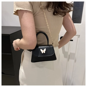 Détail du mini sac bandoulière noir avec fermoir papillon doré porté par un mannequin