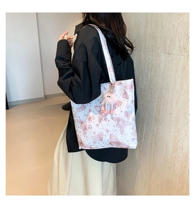 Detail van de witte draagtas met roze vlinderprints en pluche monsterbedeltje op model