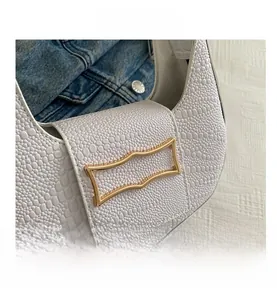 Close-up of white croc-embossed texture and golden metal buckle on a half-moon bag