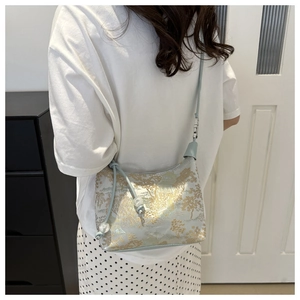 Detail of light blue crossbody bag with gold jacquard landscape pattern and beaded strap