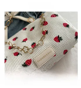 Gros plan d'un sac bandoulière en velours blanc avec motif fraise et chaîne dorée
