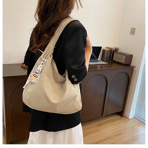 Detailansicht der beigen Canvas-Schultertasche mit Anhänger, getragen von einem Modell