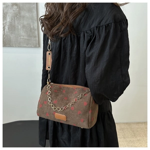 Detail der braunen Cord-Schultertasche mit Erdbeerdruck und goldener Kettenriemen