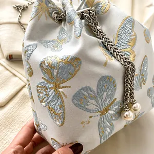 Macro detail of silk-like bucket bag featuring butterfly embroidery and pearl chain