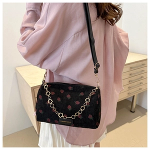 Detail of corduroy shoulder bag with strawberry print and decorative gold floral chain