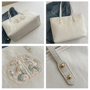 Broderie florale détaillée et rivets dorés sur un sac cabas de couleur crème