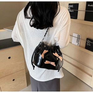 Détail d'un sac seau noir verni avec nœuds roses et bandoulière chaîne porté par un mannequin